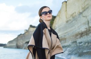 Layered Living: The Art of Year-Round Outerwear woman wearing black and brown dress and sunglasses standing near body of water under white and blue sky